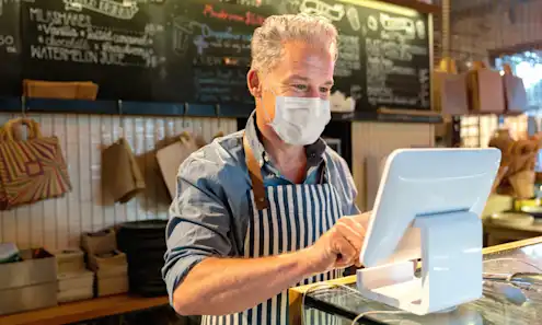 A restaurant owner using a tablet while wearing a mask