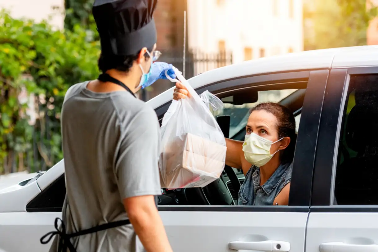 A restaurant worker delivering a to-go order to a woman in a car during COVID-19