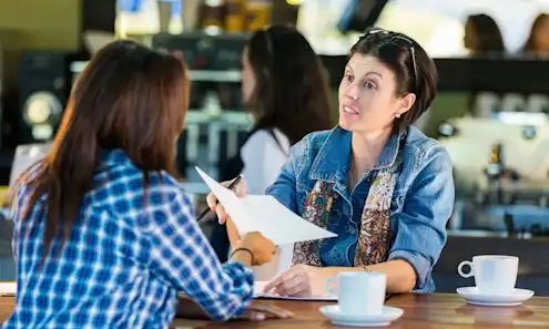 A woman interviews another woman at a coffee shop