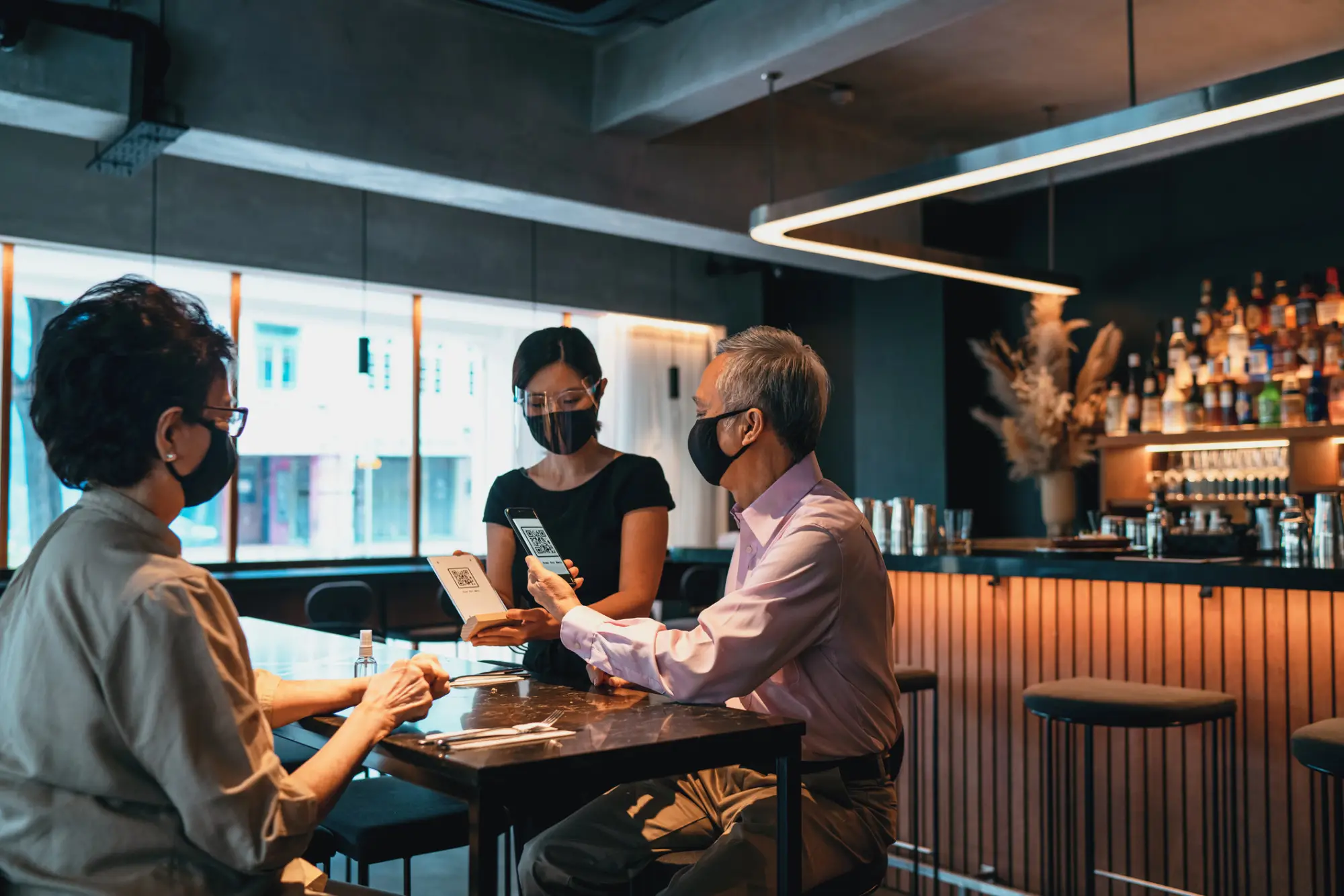 a man uses contactless dining technology by scanning a QR code at a restaurant table to view menus, order and pay.