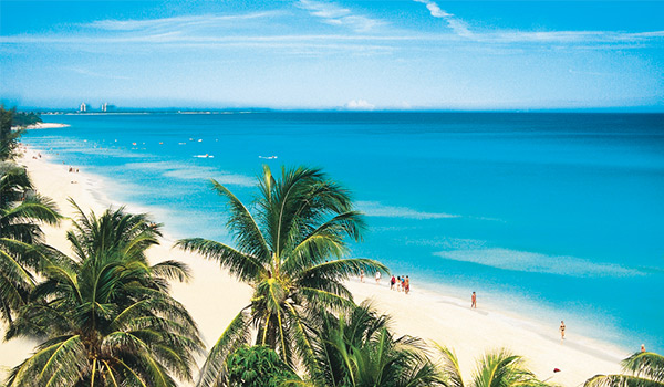 Aerial view of Varadero Beach with white-sand shores blending into bright blue waters and towering palm trees.