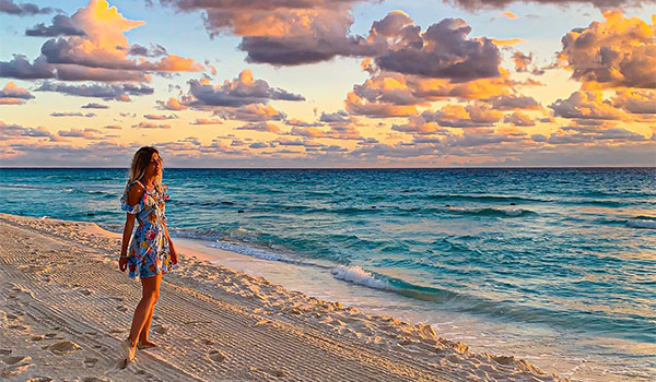 Femme portant une robe, debout sur la plage au coucher de soleil