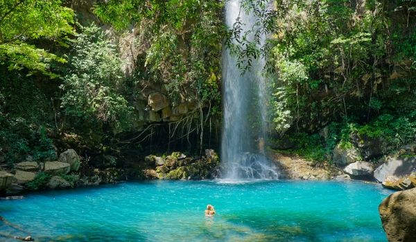 Femme nageant dans un bassin cristallin au pied d’une grande chute d’eau dans la forêt