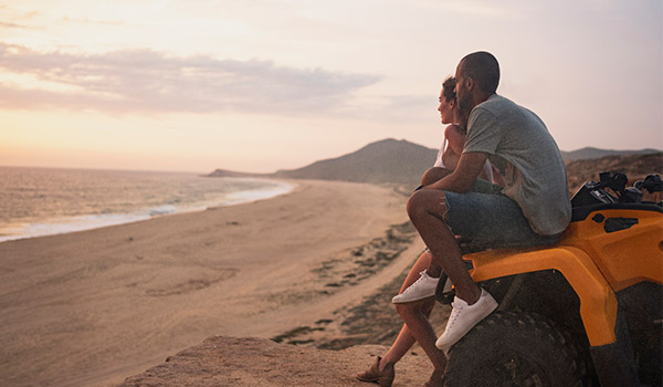 Couple sitting on an ATV overlooking the beach at sunset