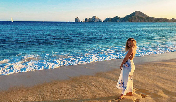 Woman standing on the beach with El Arco in the distance