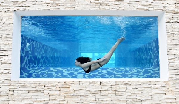 Un mur de verre à travers lequel on voit une femme qui nage dans la piscine Mermaid