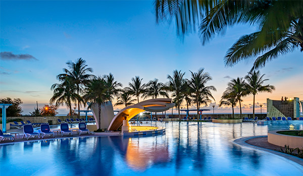 Pool area lit up at dusk with palm trees in the distance
