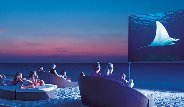 People sitting on chairs on the beach watching a movie on a projection screen