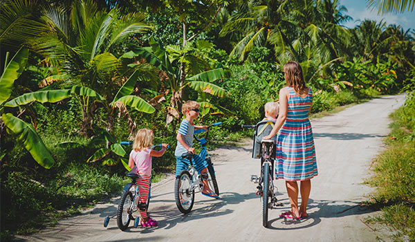 Une mère et ses trois enfants en bicycle sur un chemin bordé de palmiers