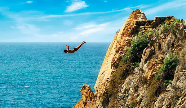 Diver jumping off a high cliff to the ocean below