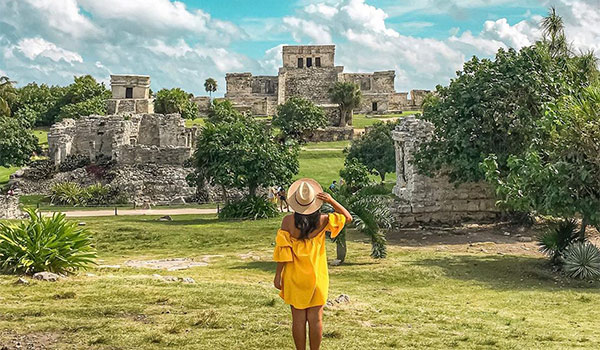 Femme avec une robe et un chapeau regardant les anciennes ruines mayas