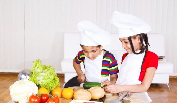 Deux jeunes enfants portant des toques blanches et préparant des légumes