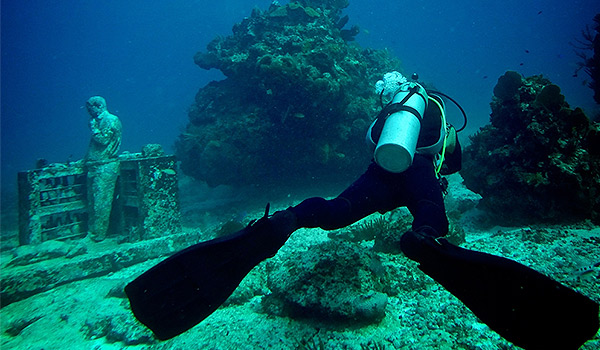 Diver swimming alongside statues at the underwater museum