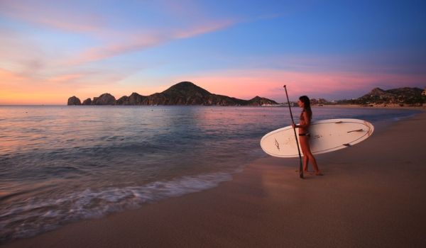 Woman holding a paddleboard at sunset in Los Cabos