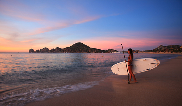 Femme tenant une planche à bras au coucher du soleil à Los Cabos