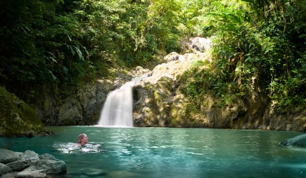 Femme se baignant dans un bassin paisible au pied d’une cascade