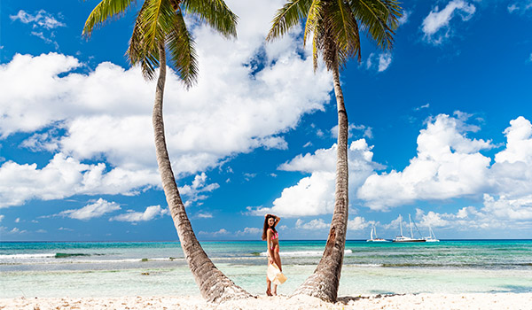 Femme debout entre deux palmiers devant la mer