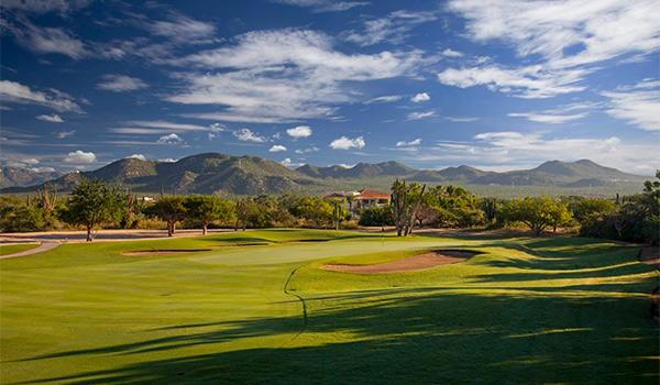 Verts immaculés d'un parcours de golf devant des montagnes à l'horizon