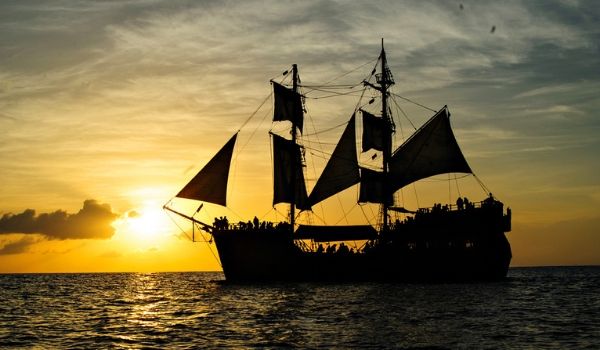 Silhouette of a pirate ship sailing through the sea at sunset
