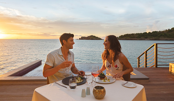 Couple eating dinner at a private table on a balcony overlooking the ocean at sunset