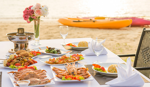 Table sur la plage recouverte de nourriture, avec des kayaks en arrière-plan