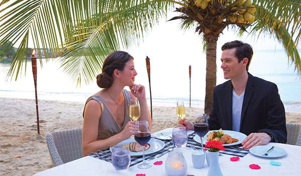 Couple enjoying a romantic dinner on the beach underneath a palm tree