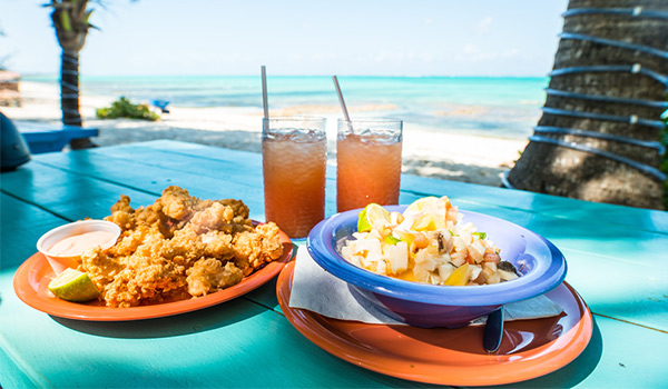 Conch fritters, conch salad and two punch drinks on a picnic table overlooking the beach