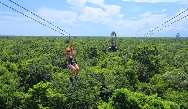 Femme en tyrolienne, en hauteur au-dessus de la canopée de la forêt tropicale