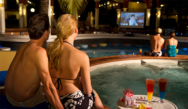 Couple sitting by the pool watching a movie on a projector screen