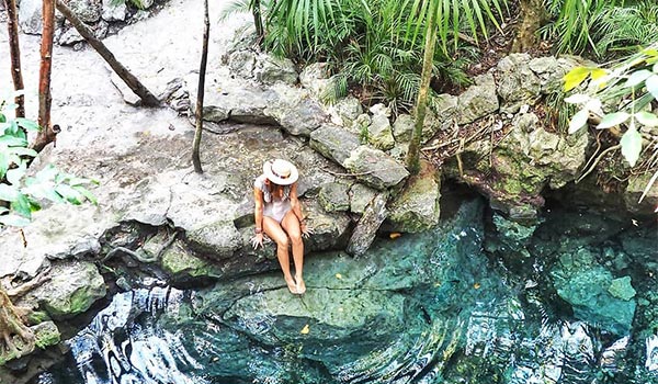 Woman sitting on the edge of a cenote in the jungle