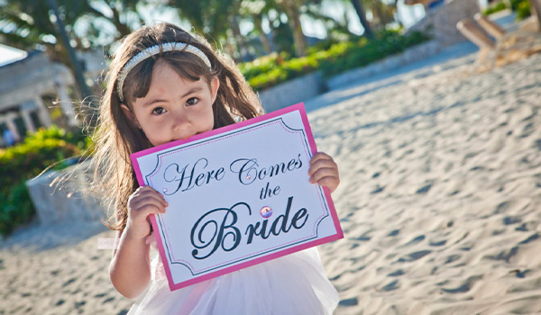 Little girl holding up a sign that says "Here comes the bride"