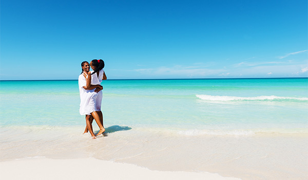 Un couple sur une plage de sable blanc, devant une mer turquoise et sous un ciel bleu