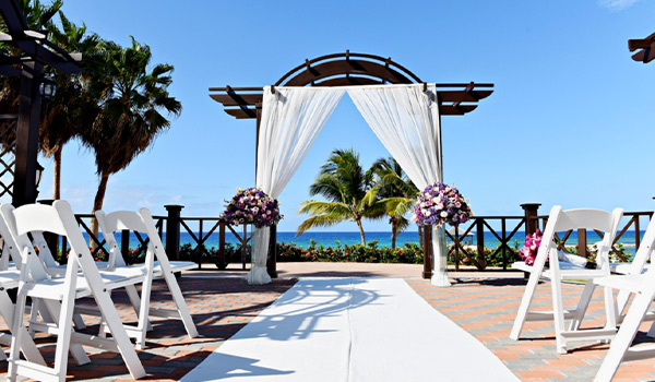 Wedding ceremony on a deck surrounded by palm trees, with the ocean in the background