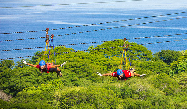 Two people ziplining above a jungle overlooking the ocean