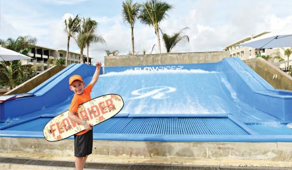 Jeune garçon avec une planche de surf devant le FlowRider