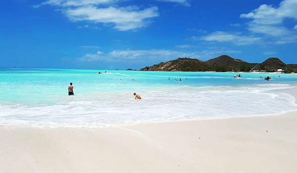 People swimming off a pristine beach with hills in the background