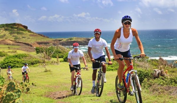 People biking up a lush hillside overlooking the coast