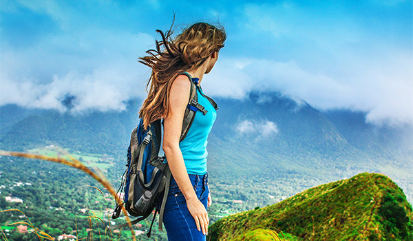 Femme portant un sac à dos regardant des paysages luxuriants à ses pieds