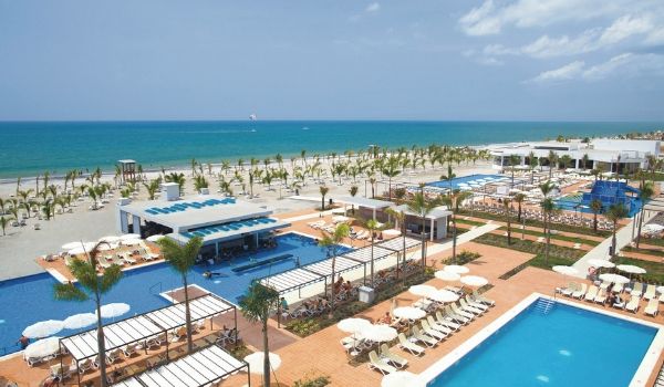 Riu Playa Blanca pool complex and swim-up bar overlooking the beach lined with palm trees.