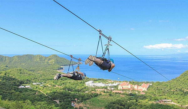 Two people Superman ziplining overlooking the coast