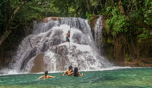 Person swinging on a rope over a waterfall into the natural pool below