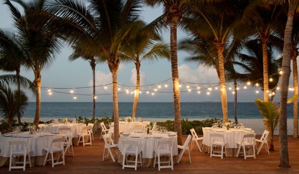 Dinner tables by the beach under twinkling lights and palm trees