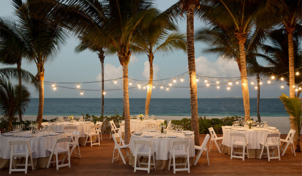 Tables pour le souper, sur la plage, sous les lumières scintillantes et les palmiers.