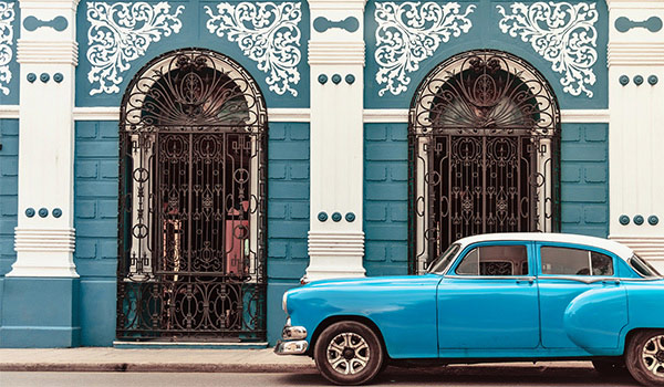 Voiture classique bleue roulant devant un mur décoré de façon unique