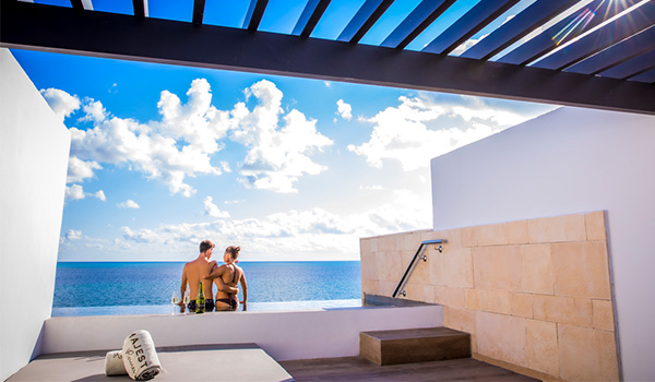 Couple sitting on the edge of a balcony infinity pool overlooking the ocean