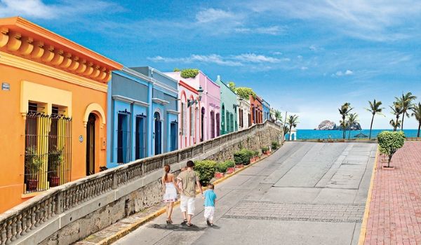 Family strolling down a coastal street lined with colourful houses