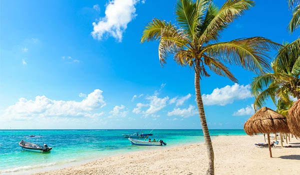 Palm trees and palapas on a pristine beach with two boats docked off the shore