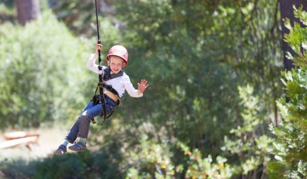 Little boy waving and ziplining through a forest