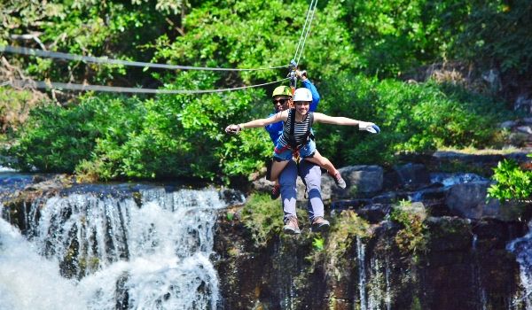 Two people tandem ziplining over a waterfall
