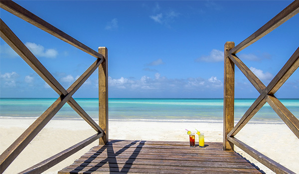 Two colourful cocktails set on a boardwalk overlooking the pristine Flamenco Beach